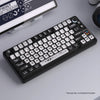 A close-up view of a black mechanical keyboard with transparent pudding style keycaps and a white laptop in the background.