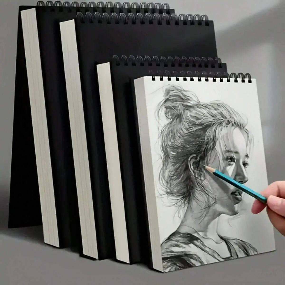 A set of black and white spiral notebooks and a sketchbook featuring a pencil drawing of a woman's profile.