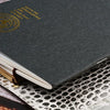 A dark gray notebook cover with gold foil text on the front, resting on a textured surface.