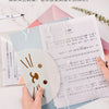 Hands are holding a set of four transparent document pouches with cartoon designs on a white marble surface.