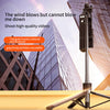 A portable Bluetooth selfie stick tripod with a fill light and remote is shown against a modern glass building.