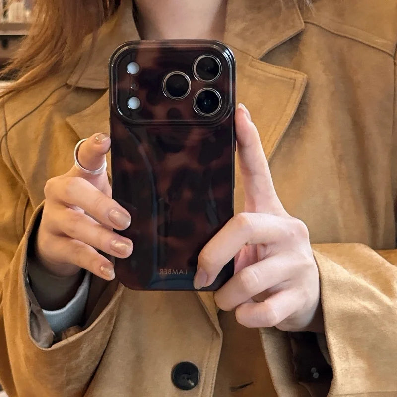 A hand holds an Amber Retro Shockproof phone case for iPhone against a brown jacket.