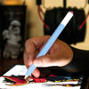 A hand holds a light blue stylus pen over a digital screen displaying artwork.