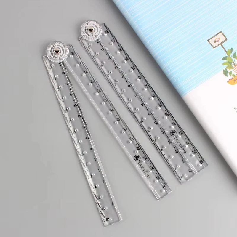 A set of precision folding transparent rulers with metal markers and a light blue striped background.