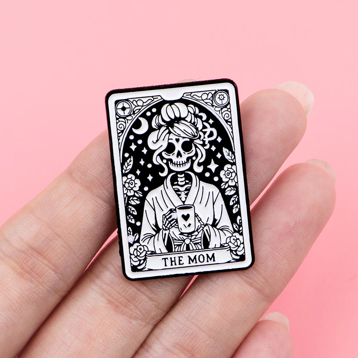 A black and white tattoo-style enamel pin featuring a skull holding a coffee cup, labeled The Mom.