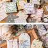 A collection of vintage floral square scrapbook paper sheets in various pastel and muted tones displayed on a wooden board.