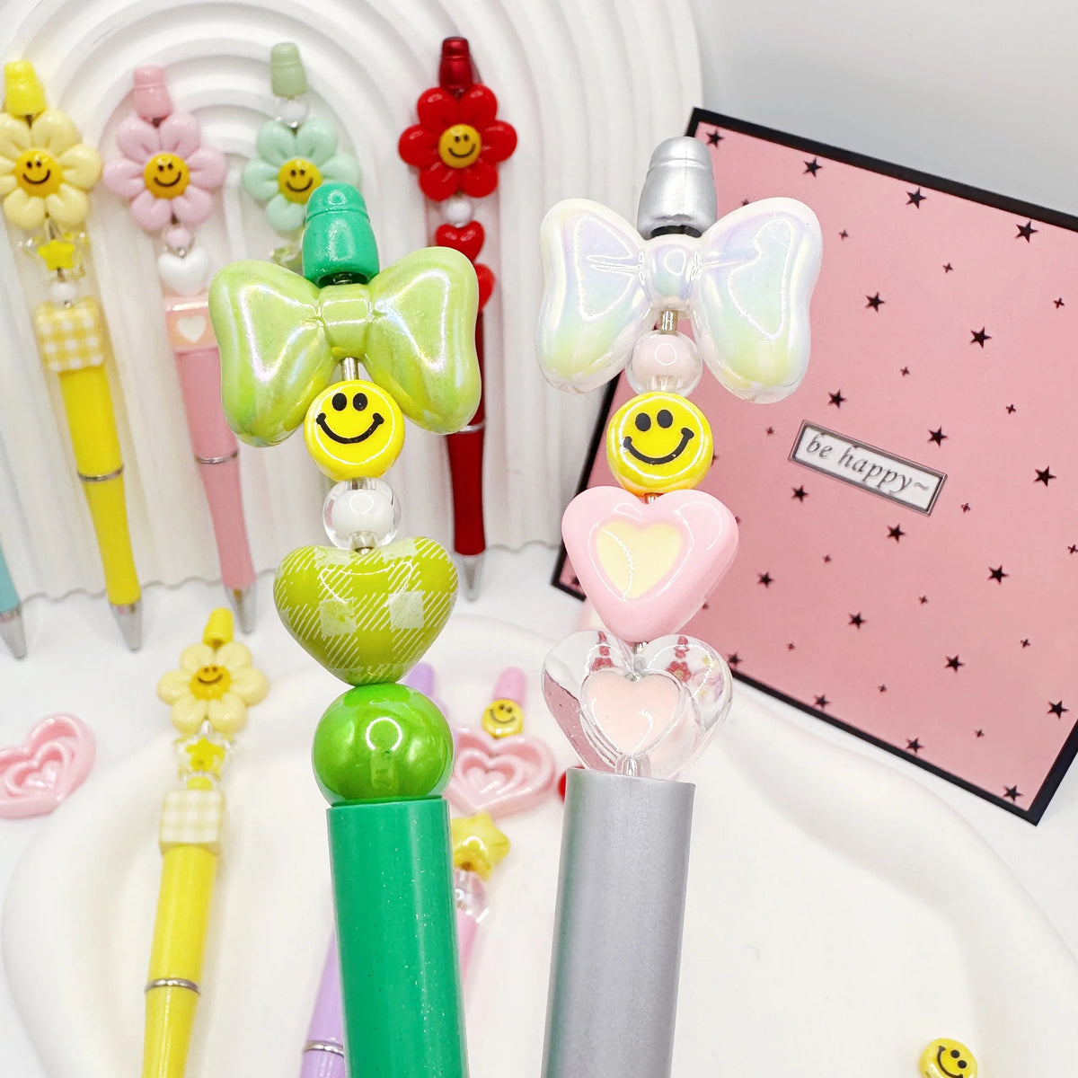 A set of colorful beaded ballpoint pens featuring heart and butterfly designs displayed in a white container.