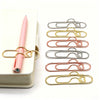 A set of gold and silver magnetic pen clips used as page markers, displayed next to a pink pen.