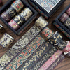 A set of metallic gold washi tape rolls featuring floral and botanical designs in dark blue and pink tones.