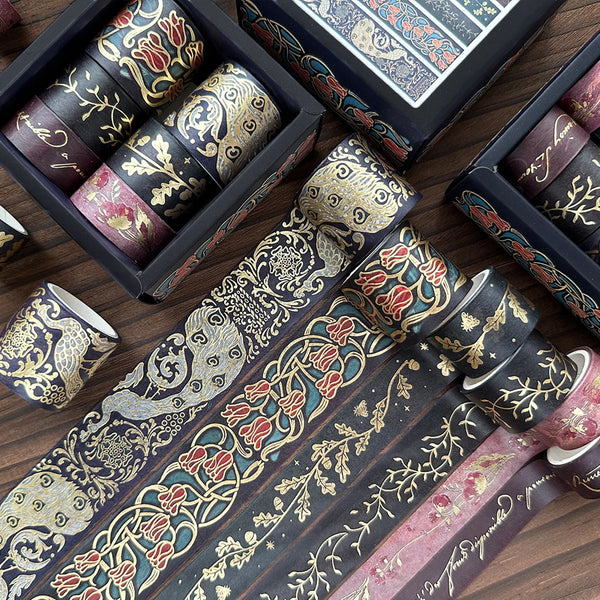 A set of metallic gold washi tape rolls featuring floral and botanical designs in dark blue and pink tones.
