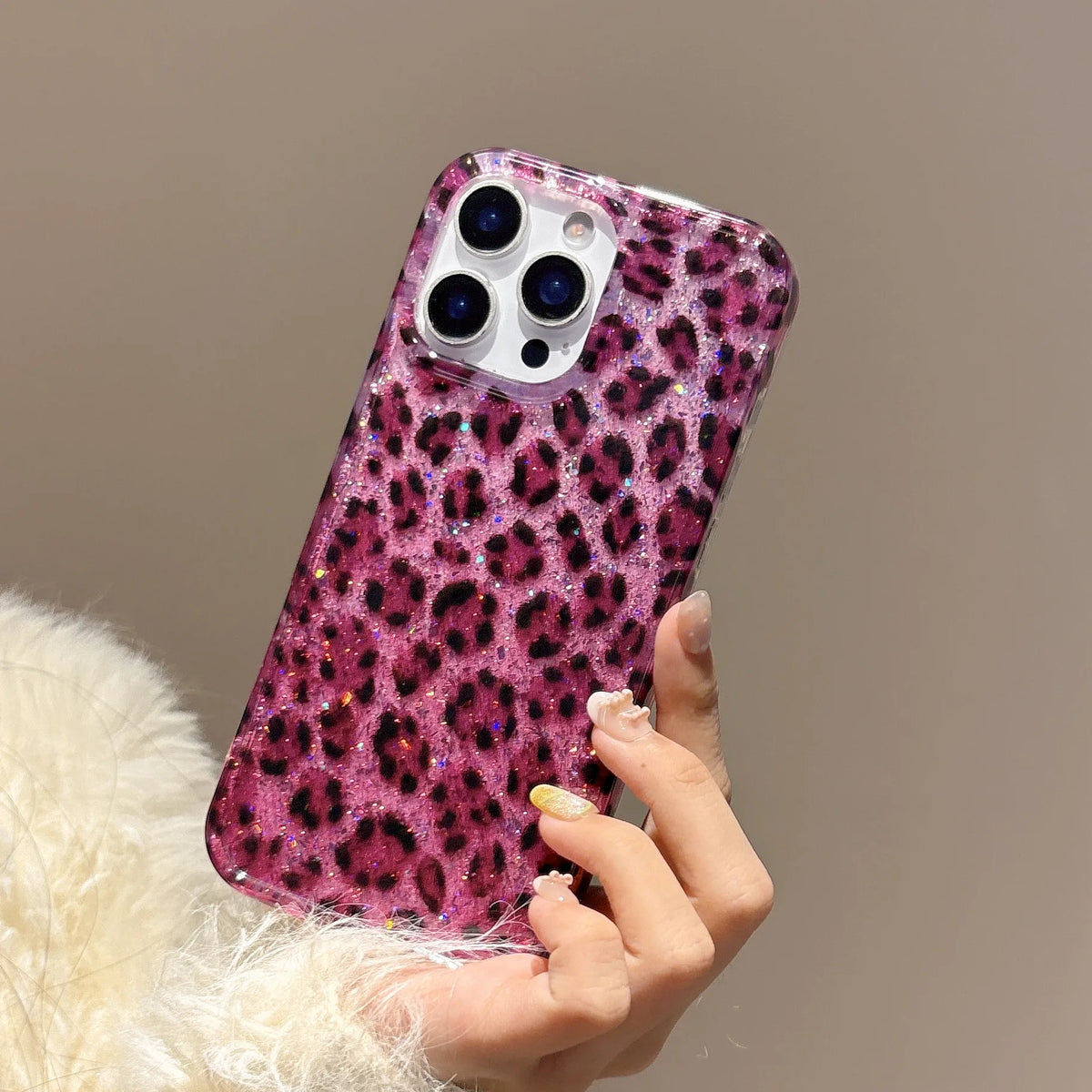 A hand holds a glamorous leopard print sequin shockproof phone case for an iPhone against a neutral background.