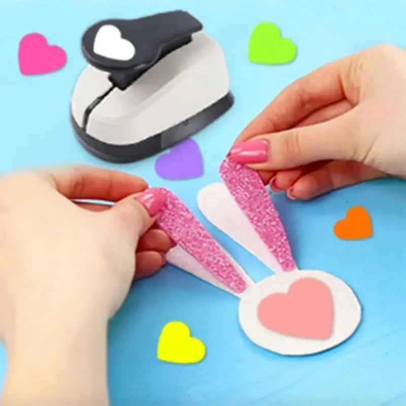Manos ensamblando una herramienta de punzón de corazón rosa con detalles de purpurina y base blanca sobre un fondo azul.