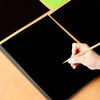 A hand is using a stylus to draw on a black scratch-off art paper sheet.