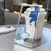 A clear plastic phone case with a floral pattern is placed next to a white tumbler.