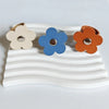 Three leather flower cable organizers in beige, blue, and orange resting on a white wavy surface.