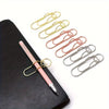 A pink magnetic pen clip with a gold-toned metal body and multiple metal clips is displayed on a black leather pad.