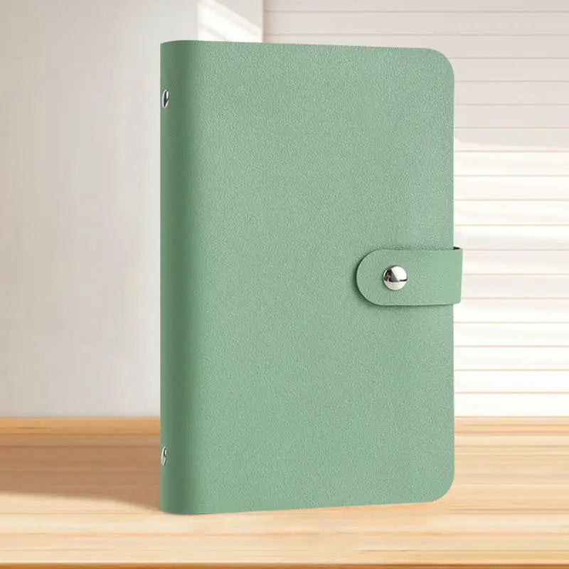A green reusable binder with a silver clasp is shown on a wooden surface.