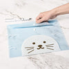 A hand places a light blue, transparent cartoon cat-shaped document pouch on a marble surface.