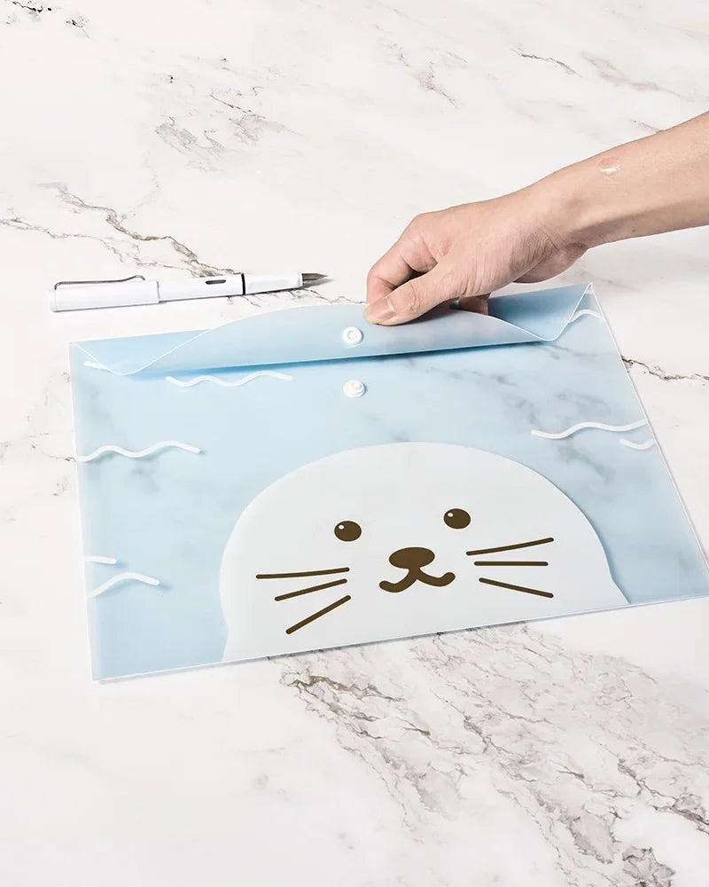A hand places a light blue, transparent cartoon cat-shaped document pouch on a marble surface.