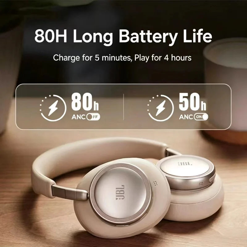A pair of beige JBL headphones resting on a wooden surface with battery life information displayed nearby.