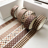 A set of six rolls of brown plaid and polka dot washi tape for crafting and journaling displayed on a white box.