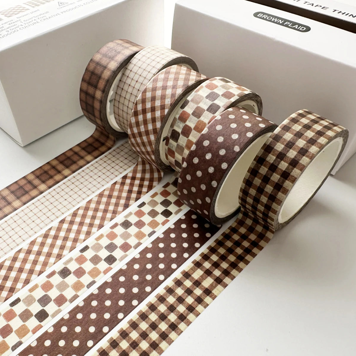 A set of six rolls of brown plaid and polka dot washi tape for crafting and journaling displayed on a white box.