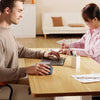 A man and a woman are working together on a laptop at a wooden table in a bright office setting.