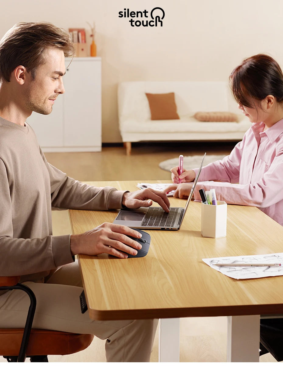 A man and a woman are working together on a laptop at a wooden table in a bright office setting.