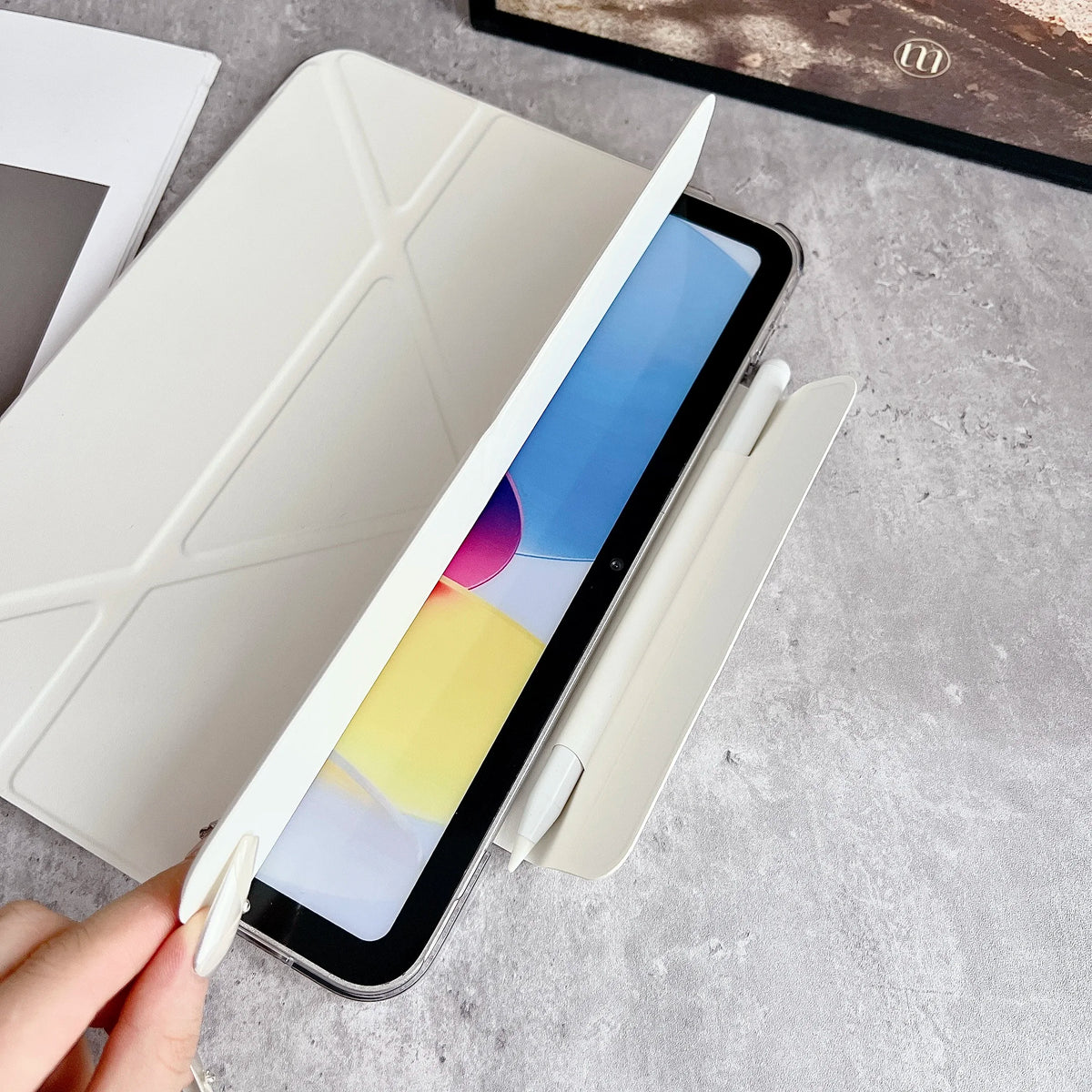 Una mano sostiene un iPad dentro de una funda protectora de cuero sintético premium, mostrando la pantalla y el cuerpo del di