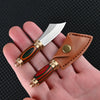 A compact fixed blade knife with a silver blade and wooden handle is shown in a brown leather sheath being held in a hand.
