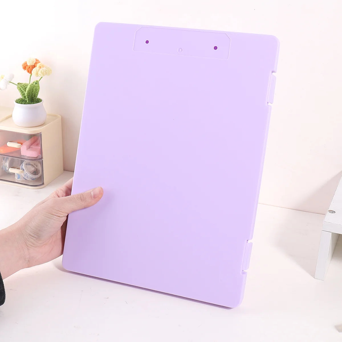 A purple A4 document and photo storage file box is shown being held by a hand on a white surface.