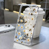 A clear phone case with a floral pattern and bees is placed next to a white cup.