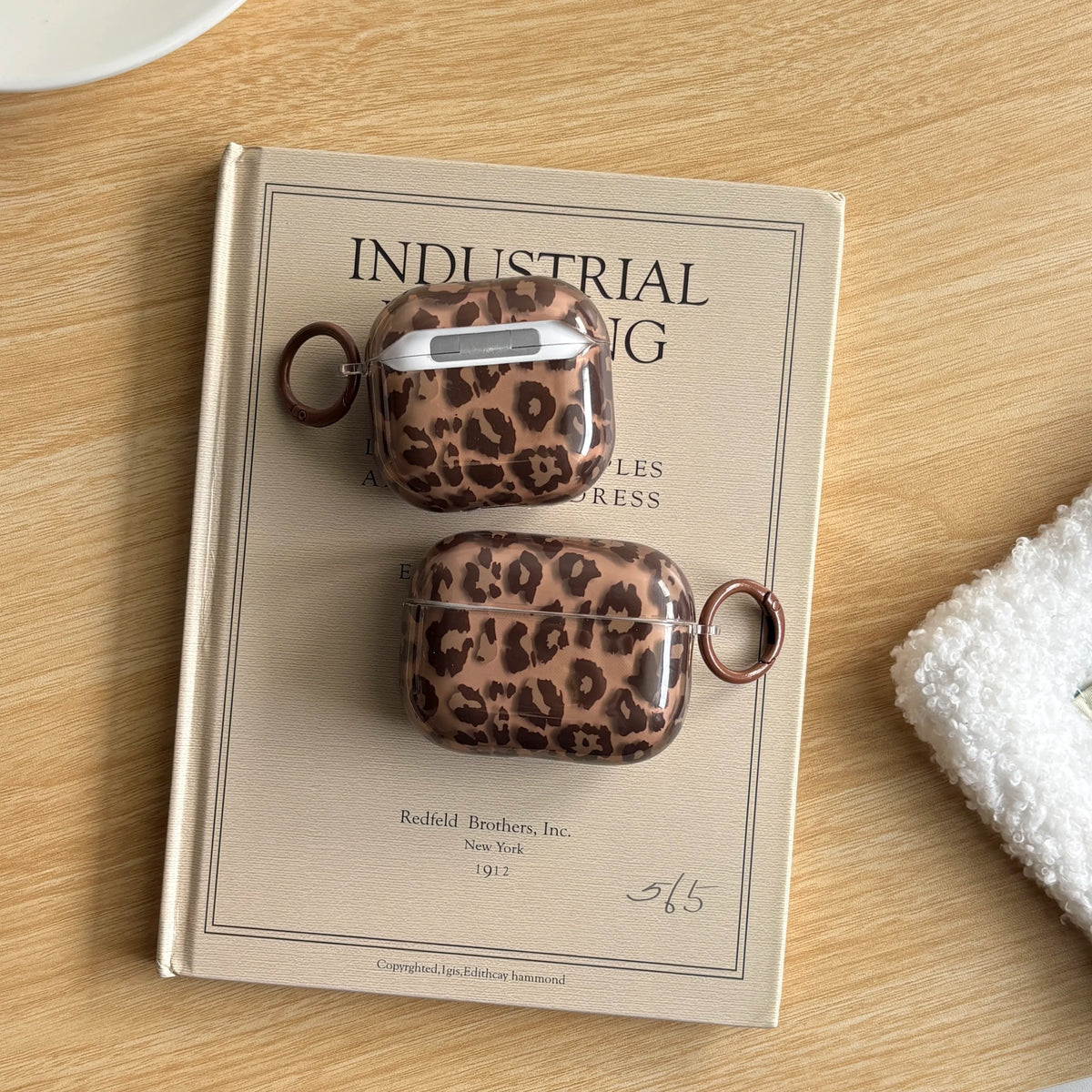 A brown leather-bound book features two leopard print earphone case covers.