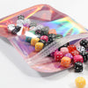 A collection of iridescent self-sealing jewelry pouches in various colors and shapes displayed inside a clear plastic pouch.