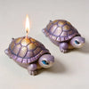 A small ceramic turtle figurine with a glowing candle on its back.