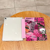 A white tablet case with a pink and black themed cover featuring various graphics and text on a wooden surface.