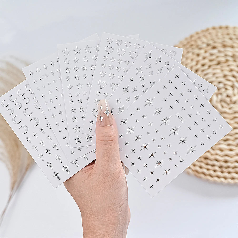 A hand holds a set of metallic 3D star nail art stickers on white cards.