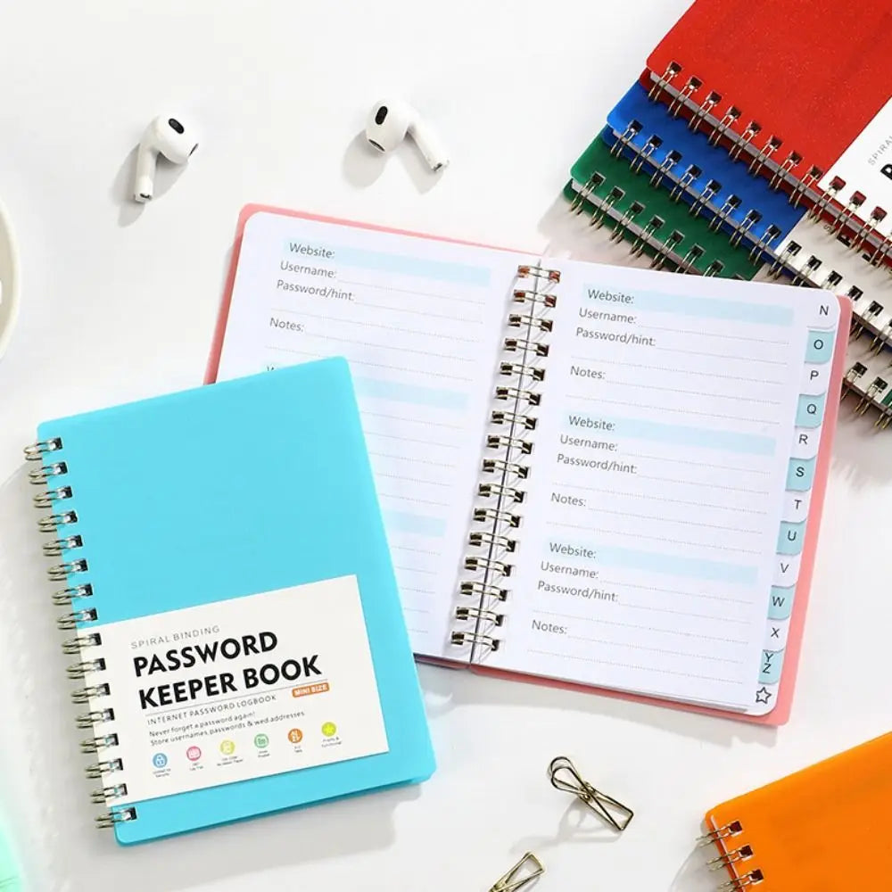 A light blue spiral-bound password keeper notebook with lined pages and alphabetical tabs is shown on a white surface.