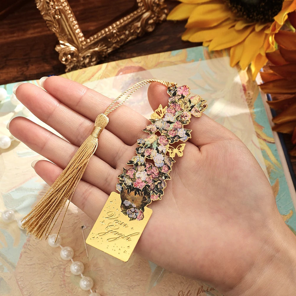 A hand holds a vintage artistic metal bookmark with a floral design and tassel on a light background.