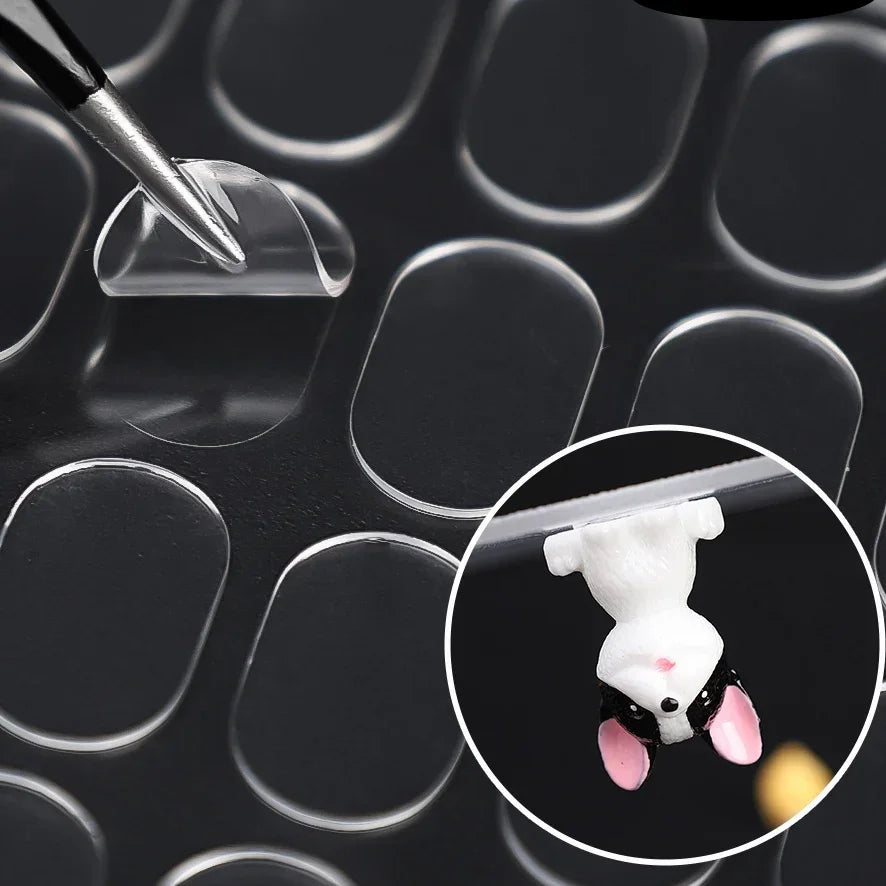 A close-up view of a white mouse figure being held by a clear adhesive pad on a dark surface.
