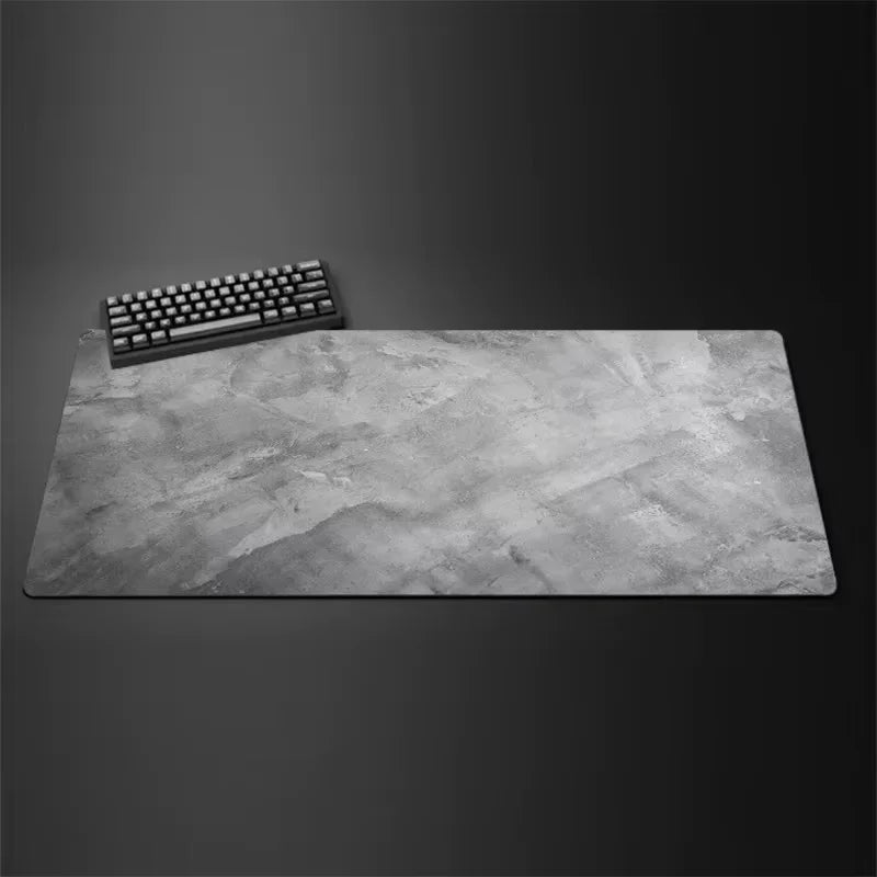 A gray overlocked mouse pad is shown on a dark surface next to a keyboard.