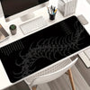Black gaming mouse pad featuring a white gothic centipede design placed on a white desk.