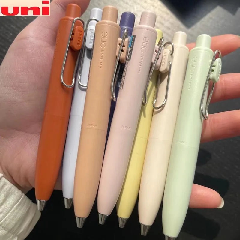 A hand holds a set of Uni-Ball One Mini cute gel pens in various pastel colors and finishes.