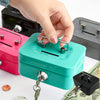 A hand is opening a teal steel cash box with a key lock and removable tray, next to some money.