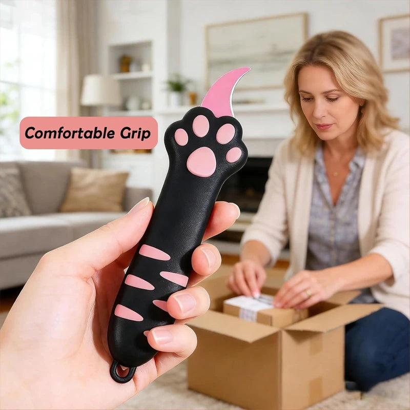 A hand holds a pink and black cat paw retractable utility knife, demonstrating its comfortable grip.