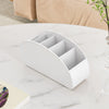 A white plastic remote control holder and desk organizer tray with multiple slots on a marble surface.