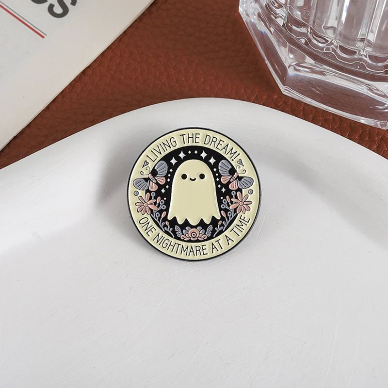 A round enamel pin featuring a white ghost with pink and black floral accents and the text Living the Dream at a Time
