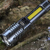 A silver tactical LED flashlight with a yellow light feature is shown outdoors in a rainy, rocky environment.