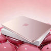 A pink Apple laptop is shown resting on a white protective case surrounded by glossy pink spheres.