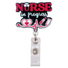 A black badge reel holder with the text NURSE in progress and a heart and ECG line design.